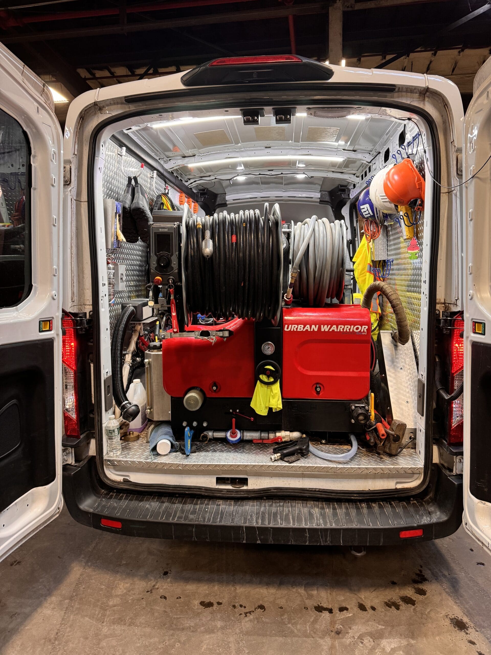 Coiled hoses, tools, and safety gear are neatly arranged around the machine, including what appears to be high-pressure hoses.